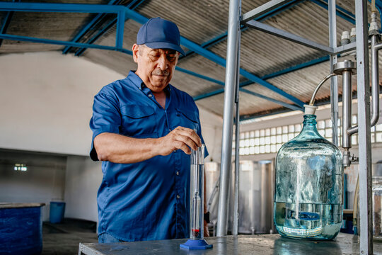 Distillery worker testing alcohol levels with a glass hydrometer tube