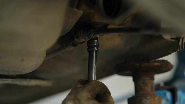 Using a socket wrench extension to unscrew a bolt under a car on a lift.