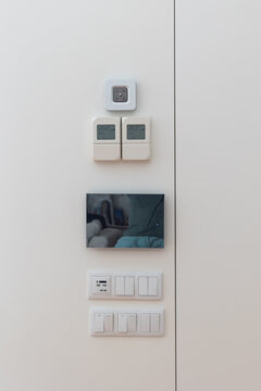 Modern smart home control panel installed on a clean white wall, featuring a touchscreen home automation display, light switches, power outlets, and digital temperature controllers.