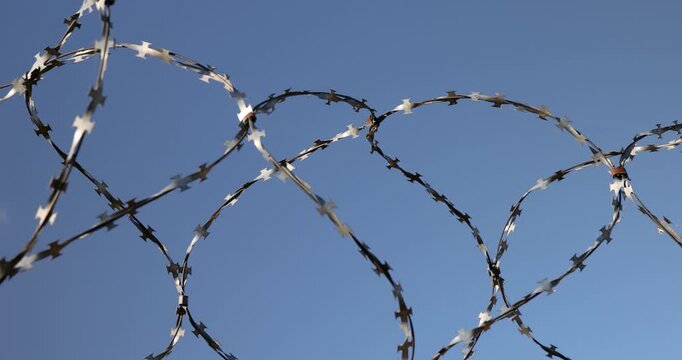   silver-tinted barbed wire against the sky, coils of reinforced barbed wire strung along the upper border of the wall