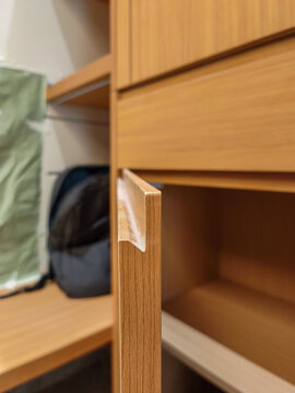 Detail of a teak wood cabinet door handle with a minimalist recessed or notched system without external metal handles on custom home interior furniture.