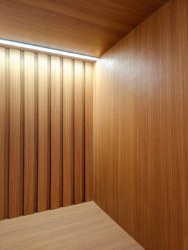 Jakarta, Indonesia - June 24, 2026: Detail of interior wall corner using vertical wood lattice panels made of brown oak HPL with hidden linear light highlights.