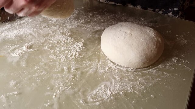 A baker's hands skillfully knead a ball of dough on a floured surface, captured in a mesmerizing slow-motion sequence
