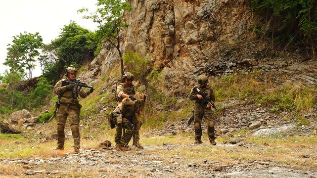  multinational soldiers in infantry uniforms, carrying paintball guns and ready for combat, run and practice military drills in a hilly, wooded area. 