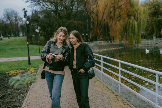 Female friends taking photos with vintage digital camera in autumn park