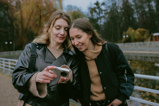 Female friends taking photos with vintage digital camera in autumn park