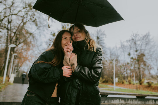 Female friends sharing umbrella on rainy autumn day in city