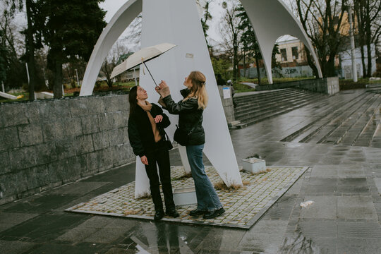 Female friends sharing umbrella on rainy autumn day in city