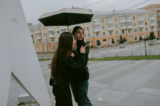 Female friends sharing umbrella on rainy autumn day in city