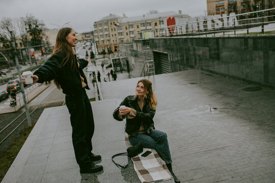 Two female friends drinking coffee outdoors on rainy autumn day