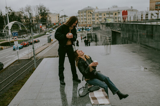 Two female friends drinking coffee outdoors on rainy autumn day