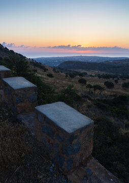 Scenic sunset over the Mediterranean sea and Analipsi town in Crete, Greece, viewed from Mount Edheri hiking trail with a stone wall and concrete pillars in the foreground creating leading lines.