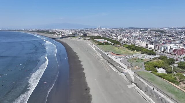 Drone Flying Forward Along Kugenuma Beach with Surfers and Coastal Cityscape, Shonan, Japan