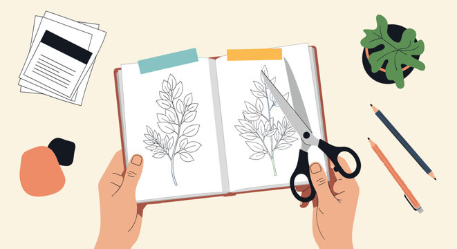 Top view of hands holding scissors to cut templates from an opened notebook on a creative workspace table.