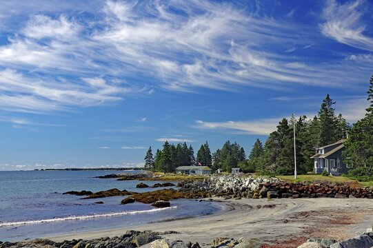A quiet beach with blue sky, white clouds, sea, sand, rocks, trees and few houses on the coast, late summer, Cherry Hill Beach, Nova Scotia, Canada