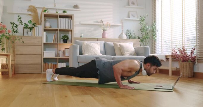 Fit Man Doing Mountain Climbers and Push-ups on Yoga Mat Following Online Workout Tutorial on Laptop at Home, Home Gym Fitness Training in Modern Living Room