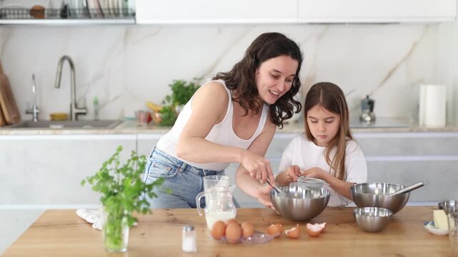 Cheerful middle-aged woman putting flour in metal bowl and whisking batter together with her daughter at home