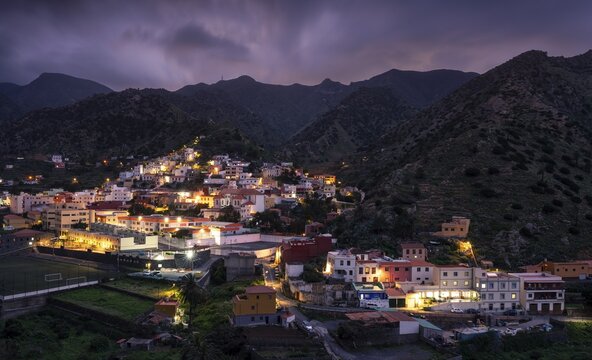 View of Vallehermoso and the surrounding mountain landscape at dusk under a cloudy sky. The street lights are switched on. Vallehermoso, La Gomera, Canary Islands, Spain