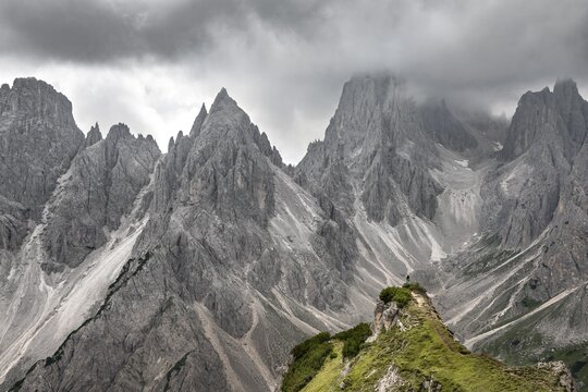 Hiker standing on a ridge, mountain peaks and pointed rocks behind, dramatic cloudy sky, Cimon di Croda Liscia and Cadini group, Auronzo di Cadore, Belluno, Italy