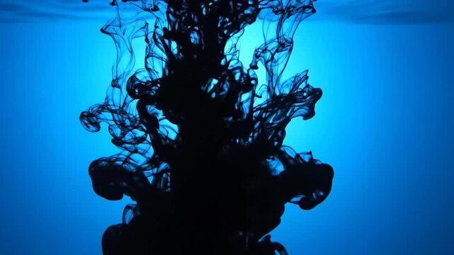 Black ink flowing and dissolving in clear water on a vibrant blue background, creating abstract shapes and textures, perfect for visual effects or motion graphics
