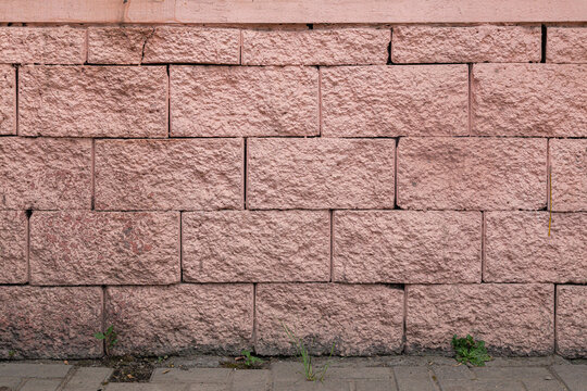 Textured background of a rough pink stone block wall. Exterior facade cladding with rusticated split-face masonry and pavement at the base.