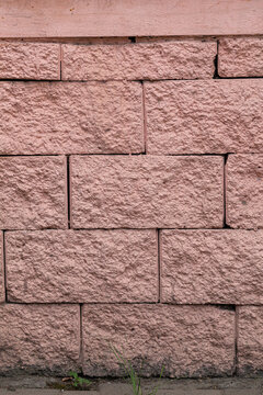 Textured background of a rough pink stone block wall. Exterior facade cladding with rusticated split-face masonry and pavement at the base.