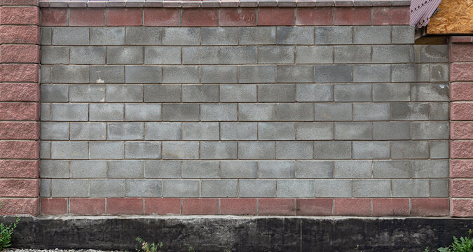 Grey concrete cinder block wall texture framed by red decorative bricks. Urban masonry background with a dark cement foundation.