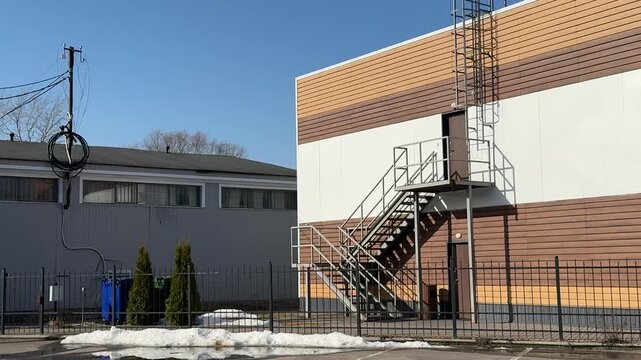 Modern building exterior with iron staircase, siding covered roof and metal ladder cage. Brown cladding over white wall