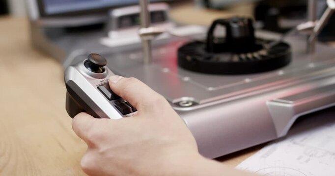 A close up view of a hand operating a handheld digital device with a joystick to control industrial machinery