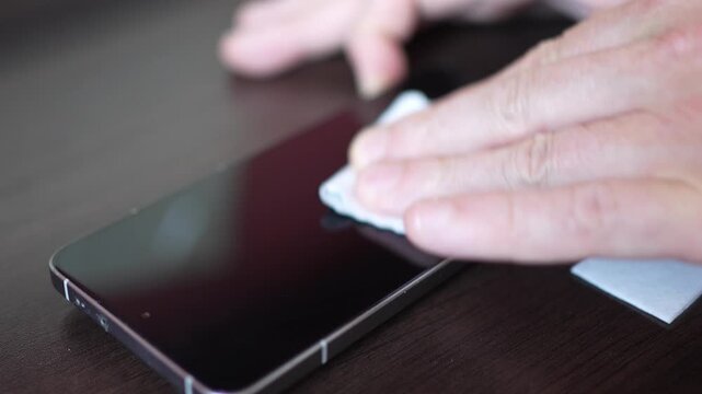 Close up of male hands wiping smartphone display with a screen cleaning wipe, preparing the glass surface for installing a new protective tempered glass or screen protector
