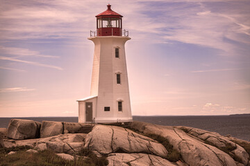 Classic white lighthouse with red lantern room stands sentinel on dramatic granite boulders overlooking calm coastal waters at golden hour. © Diana