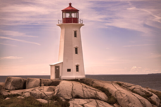 Classic white lighthouse with red lantern room stands sentinel on dramatic granite boulders overlooking calm coastal waters at golden hour.