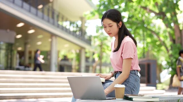 Focused asian teen girl student sitting outdoor serching on laptop writing notes in notebook distance learning studying online. college school education, e learning concept.