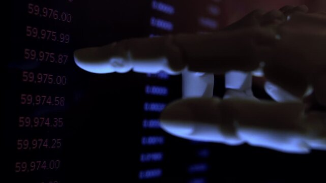 Cinematic close up of humanoid robot hand analyzing economic data from computer monitor. AI business metaphor, numbers on screen, dark office, shallow depth of field, natural dim light.