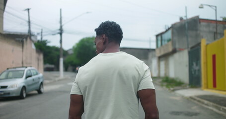 Fototapeta premium Man of African descent walking away on urban street, seen from behind, strong posture, quiet contemplation, cityscape background, muted tones, introspective, daily routine