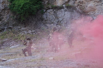 Fototapeta premium multinational group of male soldiers in infantry uniforms, carrying paintball guns and ready for combat, with pink smoke grenades and practicing military drills, with pink smoke signals 