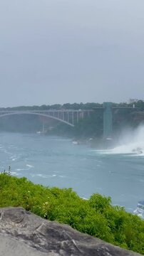 Vertical 4K ferry video at Niagara Falls with passengers, blue and turquoise water, rainbow mist, and view toward the USA side