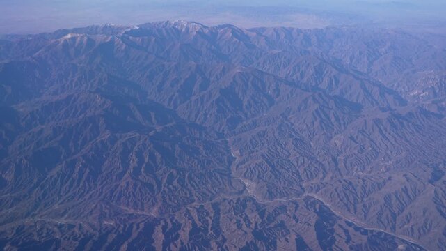 High above a massive mountain range, showing snow on the highest elevations and a river snaking through the numerous valleys at daytime
