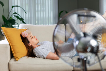 Fototapeta premium Woman resting in front of electric fan during heatwave