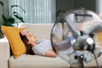 Fototapeten Pony Woman resting in front of electric fan during heatwave  © dragonstock