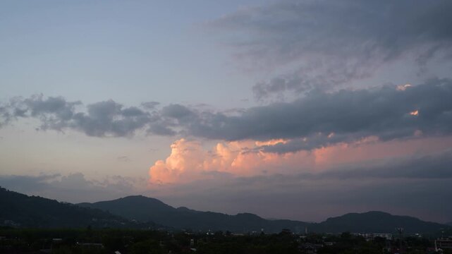 Colorful clouds shift and change shape as the sun sets behind distant mountains. Twilight hues paint the sky above a small town