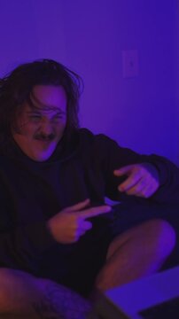 Emotional male gamer playing with controller in purple neon room