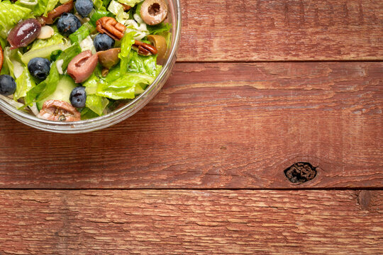 Healthy vegetable salad with romaine, olives, blueberry, cuccumber and walnuts on a rustic, weathered, barn wood table