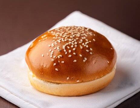 golden brown brioche burger bun topped with white sesame seeds on a white napkin