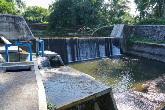 Small concrete dam with flowing water surrounded by lush green trees.