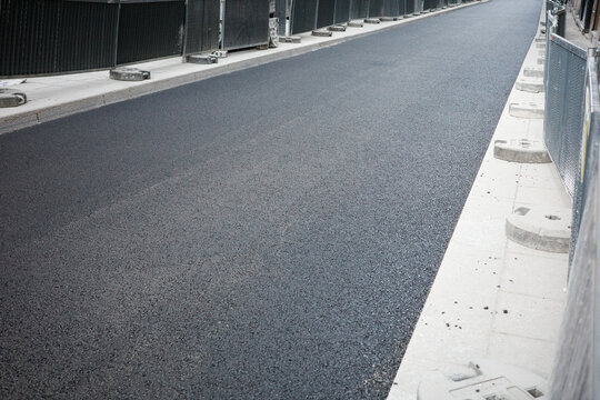 Freshly laid asphalt road flanked by construction barriers