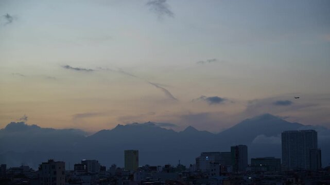 A beautiful sunset unfolds above a city with silhouetted mountains in the background, transitioning into evening twilight