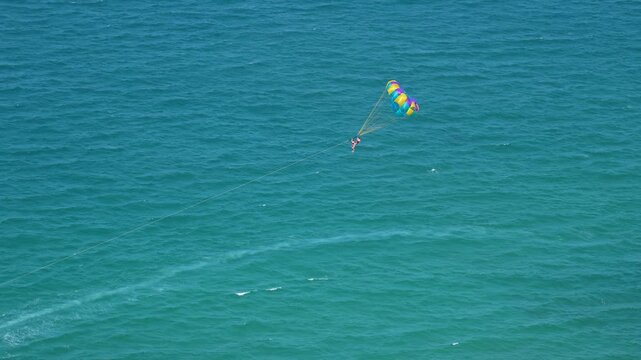 A person enjoys the exhilarating experience of parasailing over clear, blue ocean water under a bright sun, towed by a distant boat