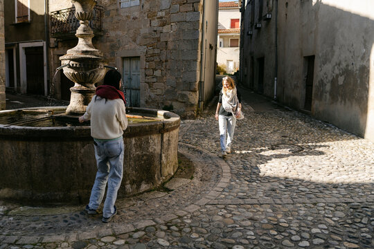 two young women playing by fountain  in village in the South of France