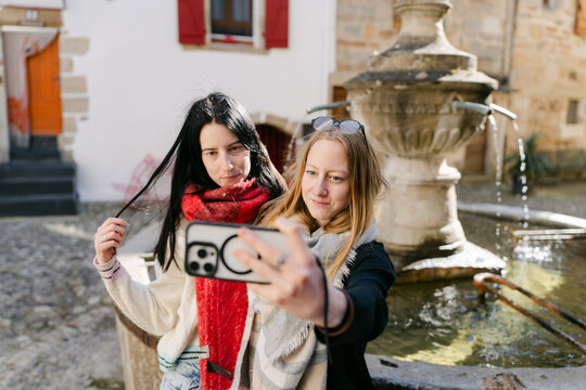 portrait of two sisters taking selfie by a fountain in France